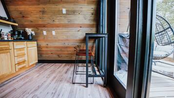 A kitchen with wooden walls, a black metal stool, and a window overlooking a deck.