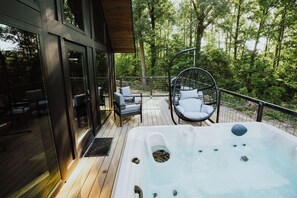 A wooden deck with a hot tub, outdoor seating, and a glass door leading to a room. - Lake Front Modern Cabin: Hot Tub, TV, & Lake Views (Cedar Bluff)