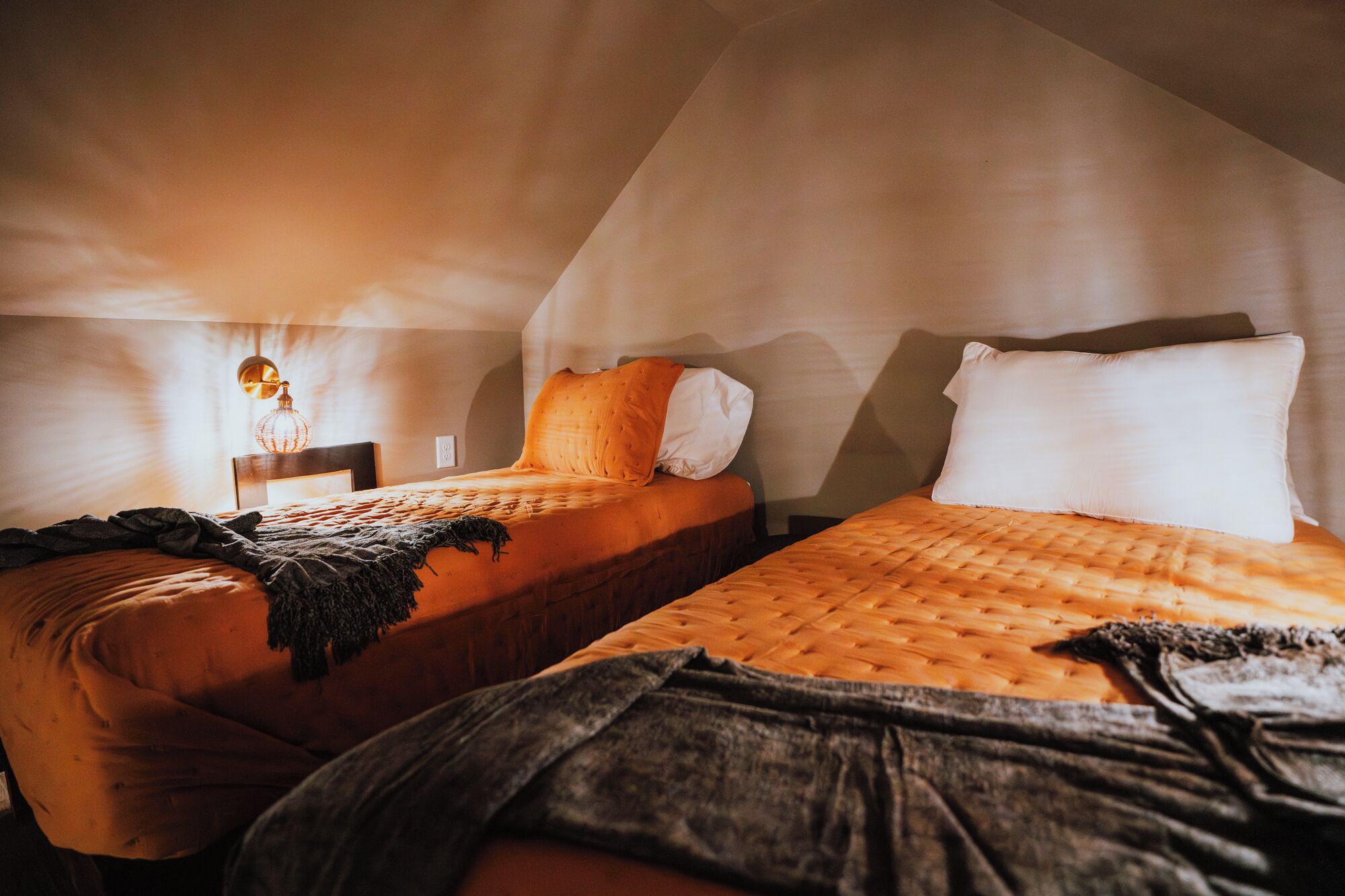 Two beds in a room with a sloped ceiling, a bedside lamp, and a blanket on one bed.
