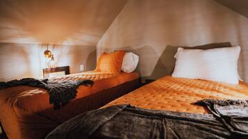 Two beds in a room with a sloped ceiling, a bedside lamp, and a blanket on one bed.