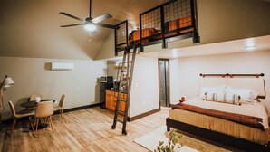 A loft-style bedroom with a bed, a desk with a chair, a ladder, a ceiling fan, and a kitchenette. - Lake Front Modern Cabin: Hot Tub, TV, & Lake Views (Cedar Bluff)