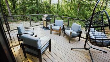 A deck with outdoor furniture, including chairs and a hanging swing, surrounded by a metal railing.
