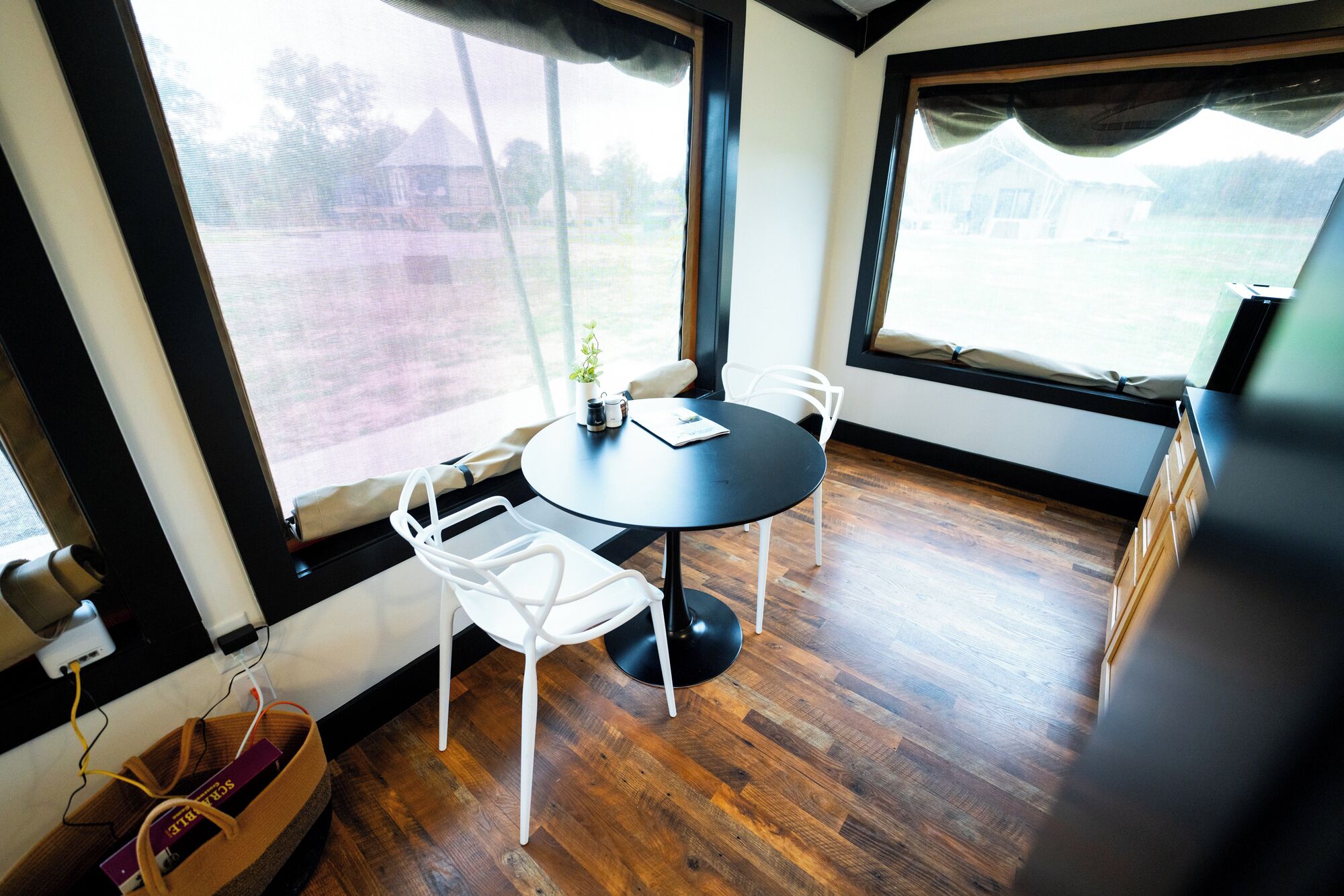 A room with a round table, two white chairs, a small potted plant, and a view of a house through large windows.