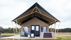 Een tentachtige constructie met een schuine kap, een deur en een klein terras met buitenmeubels.