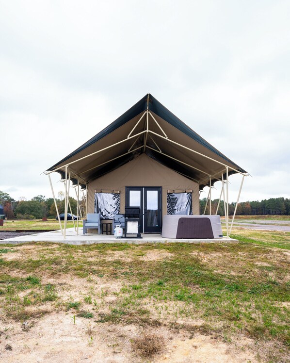 A tent-like structure with a pitched roof, a door, and a small porch area with outdoor seating.