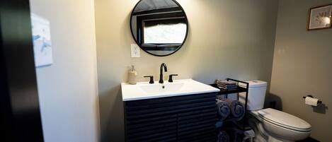 A modern bathroom with a white sink, black vanity, and a toilet.