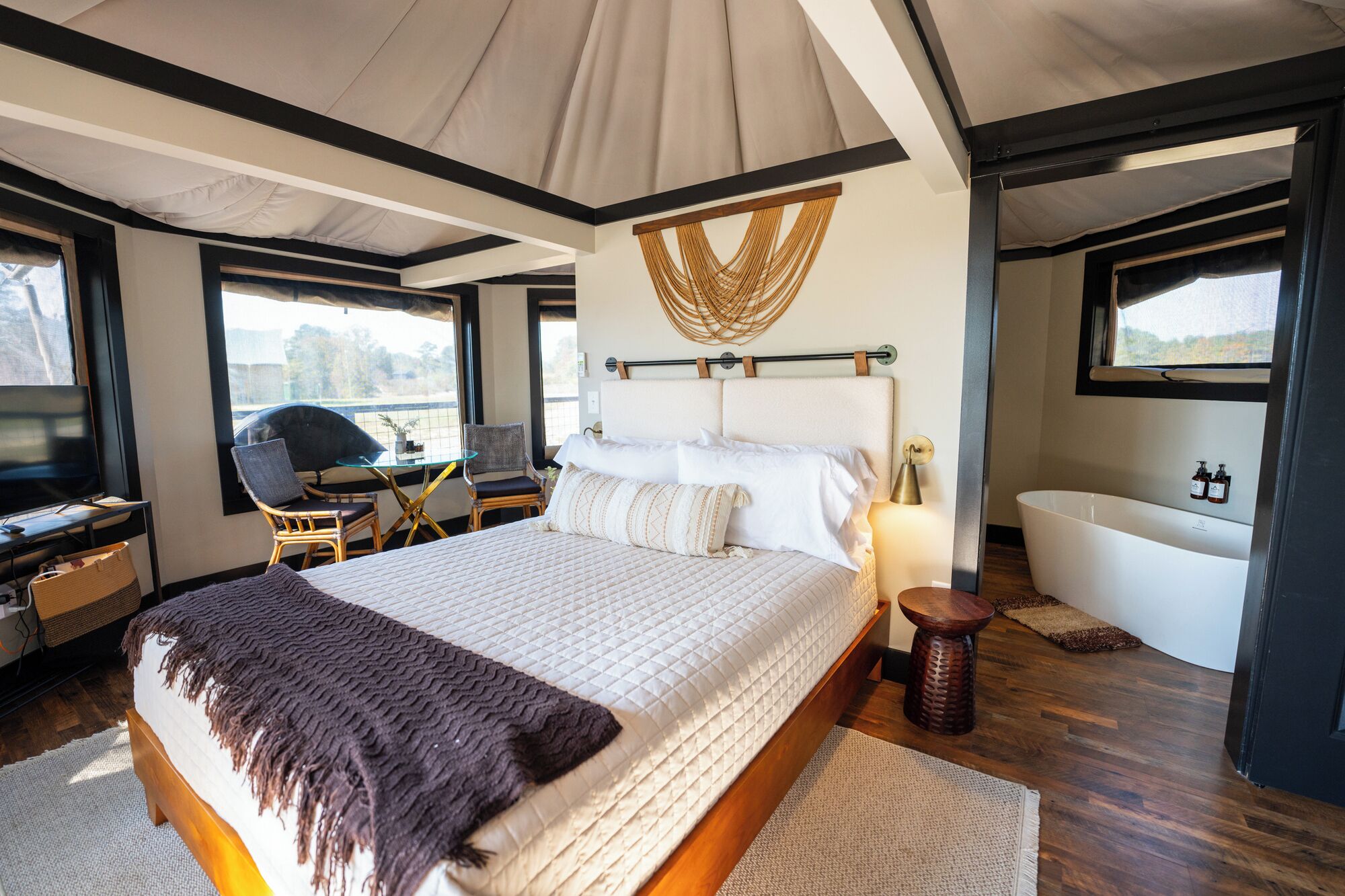A modern bedroom with a large bed, a desk with a chair, a television, and a view of the outdoors.