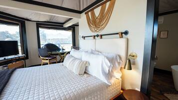 A bedroom with a large bed, a desk with a chair, and a window.