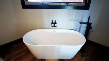 A modern bathroom with a freestanding bathtub, a window above the sink, and two bottles of hand soap on the wall.