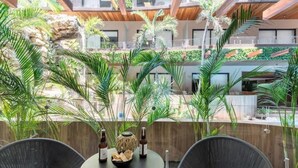 Un espace extérieur moderne, aménagé avec des fauteuils en osier et une table ronde, entouré d’une végétation luxuriante et d’un mur en pierre.