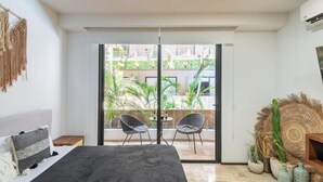 Une chambre avec un lit, un balcon avec des chaises et une vue sur la verdure environnante.