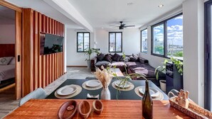 Ein modernes Wohnzimmer mit Essbereich, großen Fenstern und einem Deckenventilator.