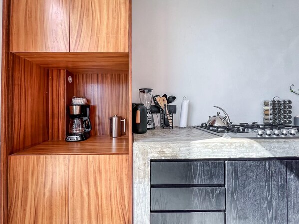 A modern kitchen with wooden cabinets, a coffee maker, a kettle, a blender, and a gas stove.