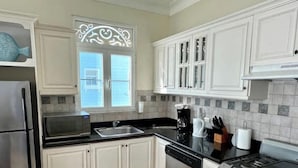 Una cocina con armarios blancos, un refrigerador de acero inoxidable, un lavavajillas, una estufa y una ventana con detalles decorativos.