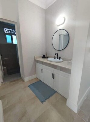 A bathroom with a white sink, black faucet, and a round mirror. There is a blue rug on the floor and a door leading to another room. - D-1 Rest & Relax at The Victorian (Cabarete)