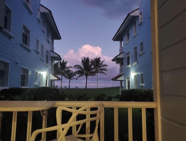 A view of a hotel corridor with two-story buildings, palm trees, and a balcony with a chair. - D-1 Rest & Relax at The Victorian (Cabarete)