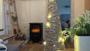 Un salon chaleureux avec une cheminée, un sapin de Noël décoratif et un téléviseur fixé au mur.