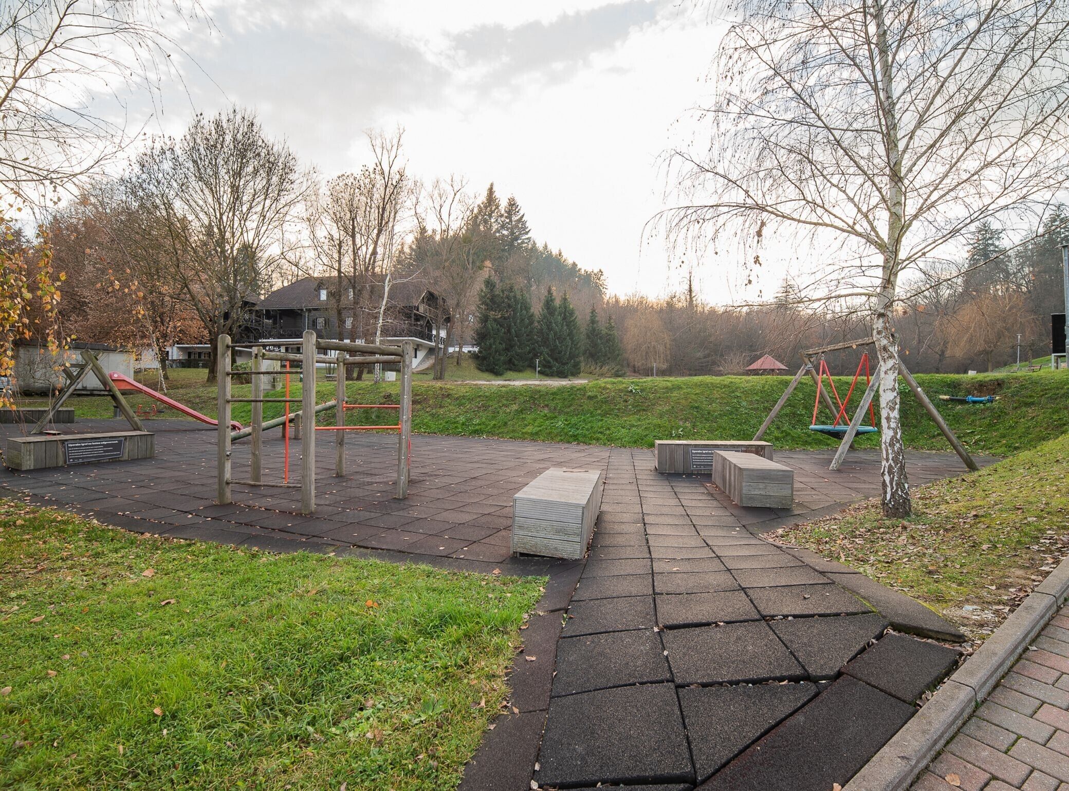 A playground with swings and climbing structures, surrounded by grass and trees.