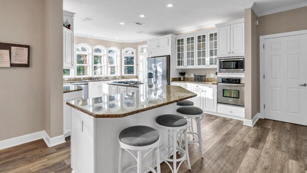 A modern kitchen with white cabinetry, a granite island with bar stools, and a large window providing natural light. - Private Pool 🏊 Walk to Beach 🏖️ Family Tides 🏝️ (Destin)