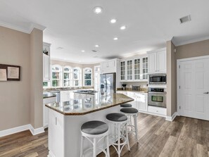 A modern kitchen with white cabinetry, a granite island with bar stools, and a large window providing natural light.