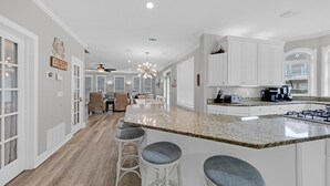 A modern kitchen with white cabinetry, a granite countertop, and bar stools. - Private Pool 🏊 Walk to Beach 🏖️ Family Tides 🏝️ (Destin)