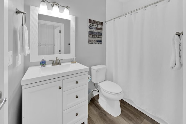A bathroom with a white vanity, a mirror with lights, a toilet, and a shower curtain.