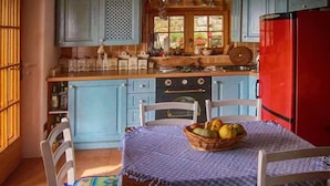 Eine Küche mit hellblauen Schränken, einem roten Kühlschrank, einem Holztisch mit Obstkorb und weißen Stühlen.