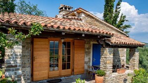 Ein rustikales Steinhaus mit Ziegeldach, Holztüren und einer kleinen Veranda mit Blumentöpfen.