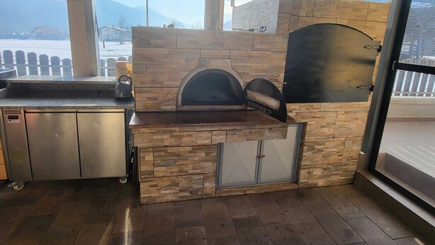 Una cucina esterna con forno in pietra, lavello in acciaio inossidabile e vista sulle montagne.