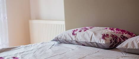 Una cama con cubrecama y almohadas de estampado floral, un cabecero sencillo y un radiador blanco al fondo.