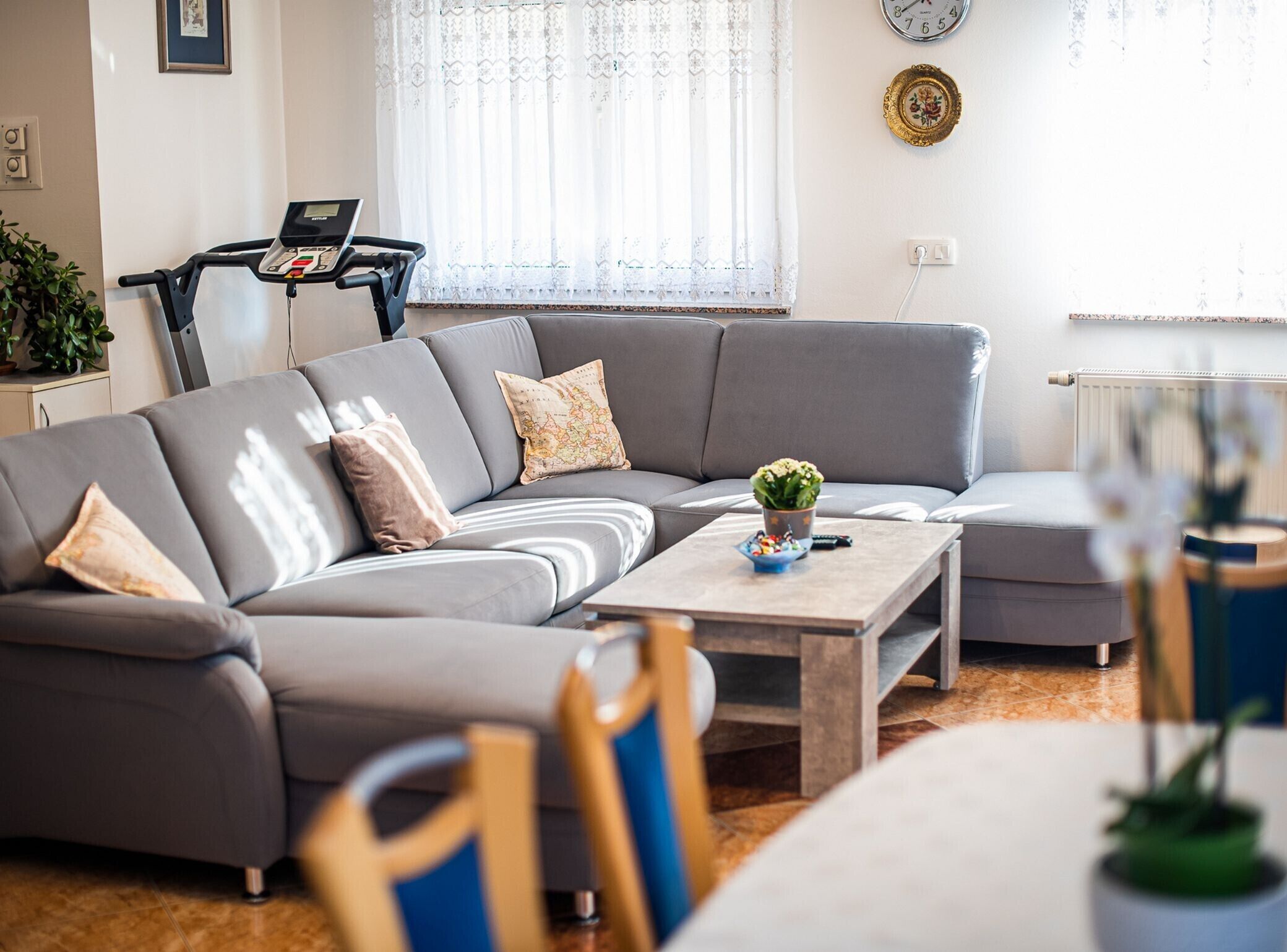 A modern living room with a grey sectional sofa, a coffee table, and a treadmill in the background.