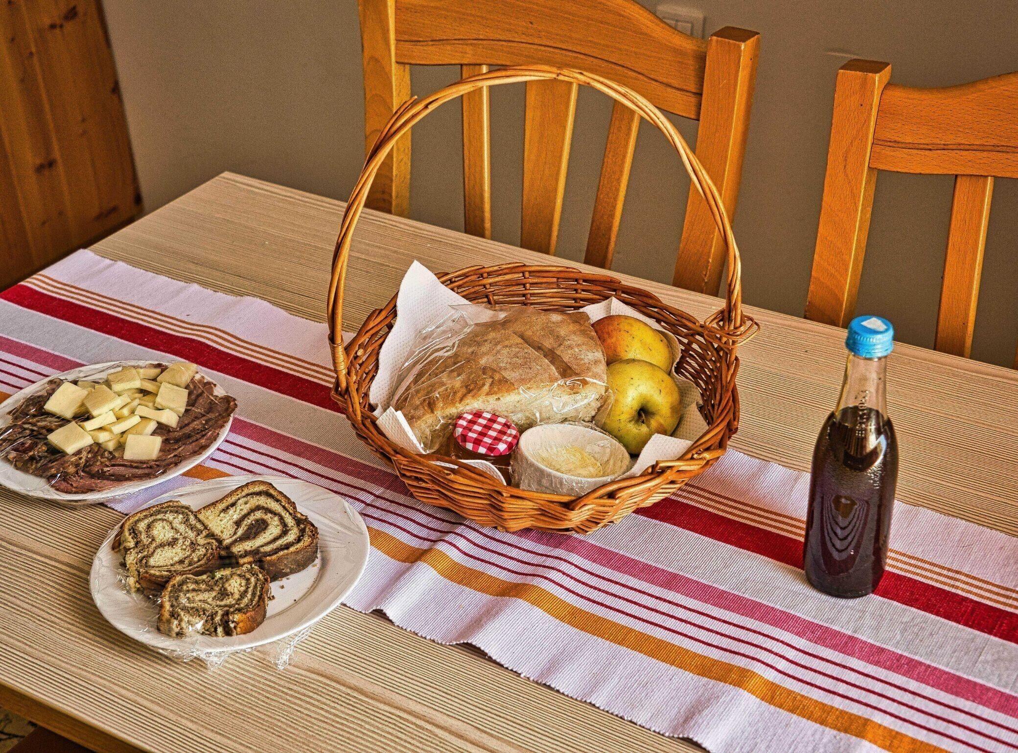 Ett bord med ett randigt bordsduk, en korg av rotting som innehåller bröd, äpplen och ett smörpaket, och två tallrikar med bakverk.