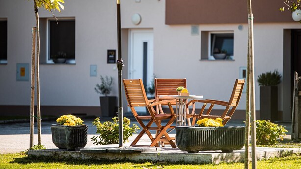 An outdoor seating area with a wooden table and chairs, a red umbrella, and potted plants.