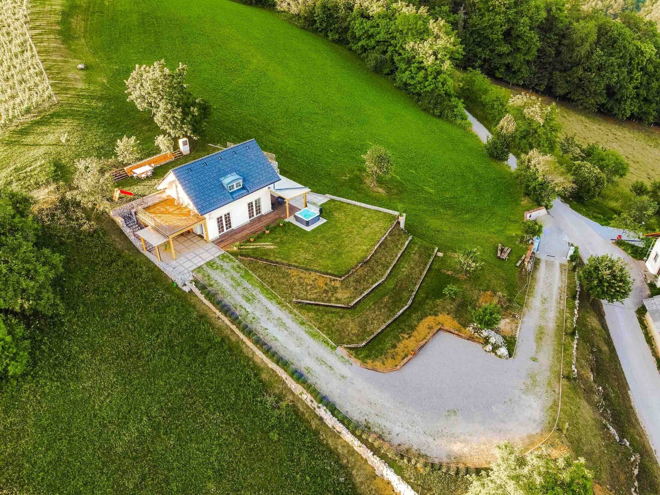 Vue aérienne d’une maison avec un toit bleu, entourée d’une pelouse bien entretenue et d’un petit étang.