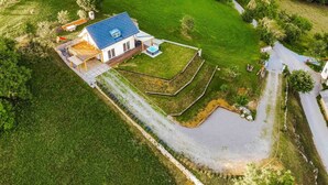 Vue aérienne d’une maison avec un toit bleu, entourée d’une pelouse bien entretenue et d’un petit étang.