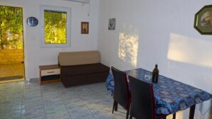 Een lichte, kleine kamer met betegelde vloer, een bank, een tafel met stoelen en een raam.