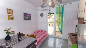 A compact living space with a dining area, a bed, a ceiling fan, a window with a curtain, and a view of the outside.