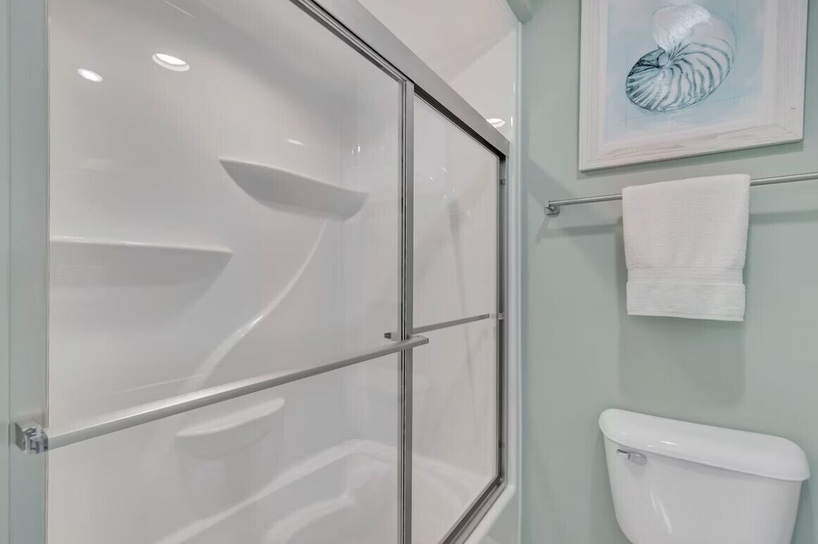 A modern bathroom with a glass shower enclosure, a white toilet, and a framed artwork on the wall.