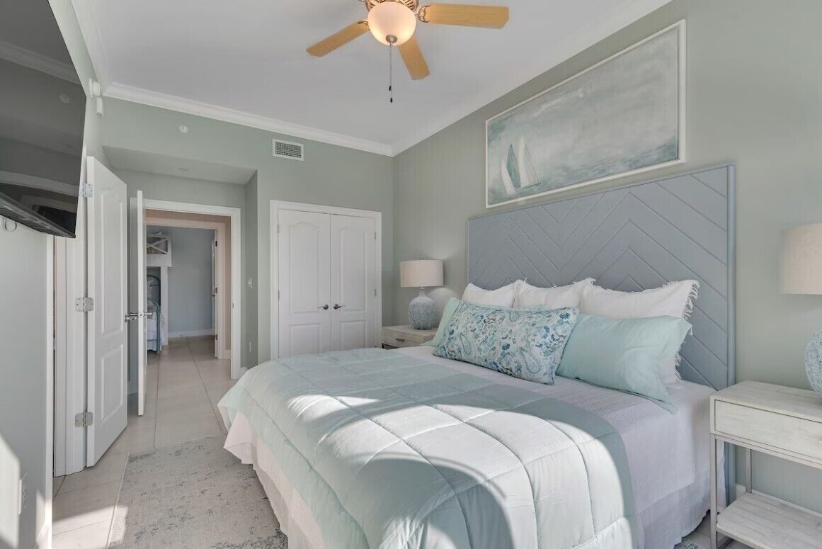 A bedroom with a bed, a ceiling fan, a nightstand, and a door leading to another room.