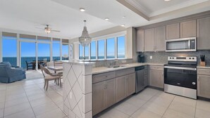 A modern kitchen with large windows, a dining area with a view, and a ceiling fan. - Luxury 4BR Beachfront Corner Unit, Panoramic Gulf Views, Lazy River, Indoor Pool (Orange Beach)