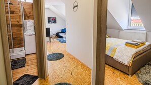 Un dormitorio moderno con techo inclinado, una cama con colcha de estampado geométrico, una mesita de noche y una ventana con vistas a edificios.