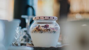 A clear glass bowl with a decorative lid containing yogurt and granola.