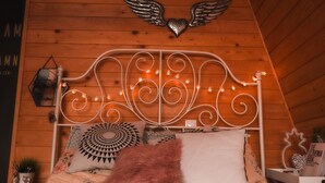 A wooden-paneled room with a metal bed frame, decorative pillows, and string lights.