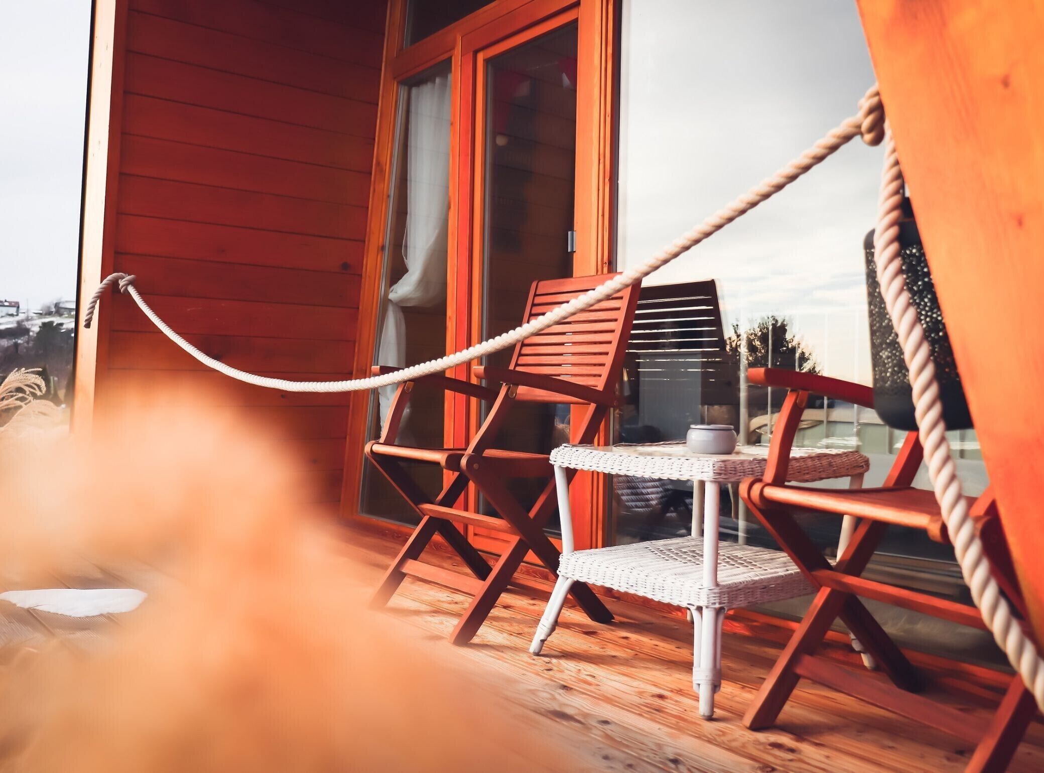 A wooden deck with two wicker chairs and a small table, connected by a rope.