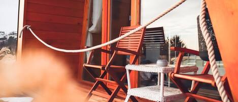 A wooden deck with two wicker chairs and a small table, connected by a rope.