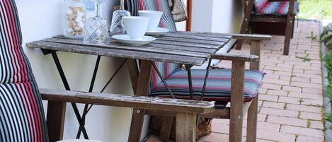 A rustic outdoor seating area with a wooden table and chairs, a white pitcher, and a glass jar with sugar cubes.