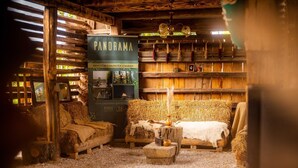 A rustic room with wooden furniture, hay-covered floors, and a wooden wall with a sign reading "PANORAMA".