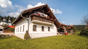 Una casa a due piani con un balcone, un portico in legno e un giardino.