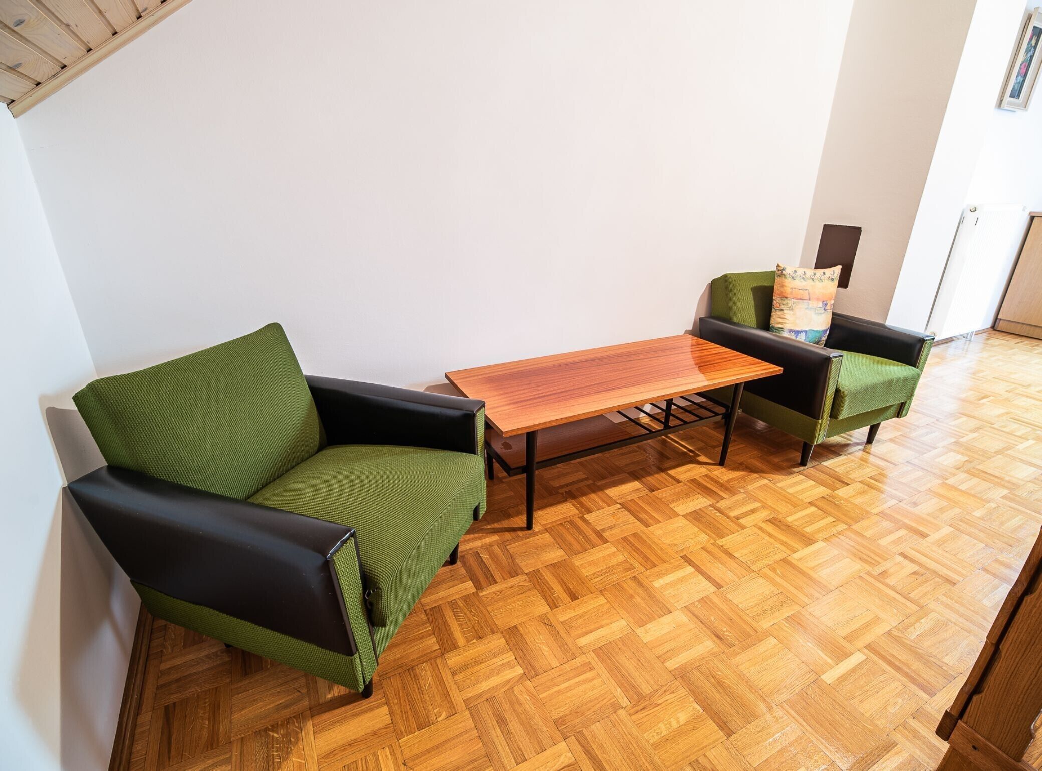 A room with a herringbone wooden floor, two green armchairs, and a wooden coffee table.