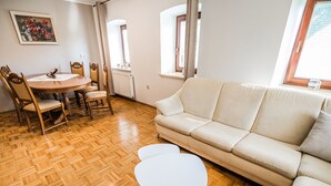 Un soggiorno con pavimento in parquet in legno, un divano beige, un tavolino bianco e un tavolo da pranzo con sedie.